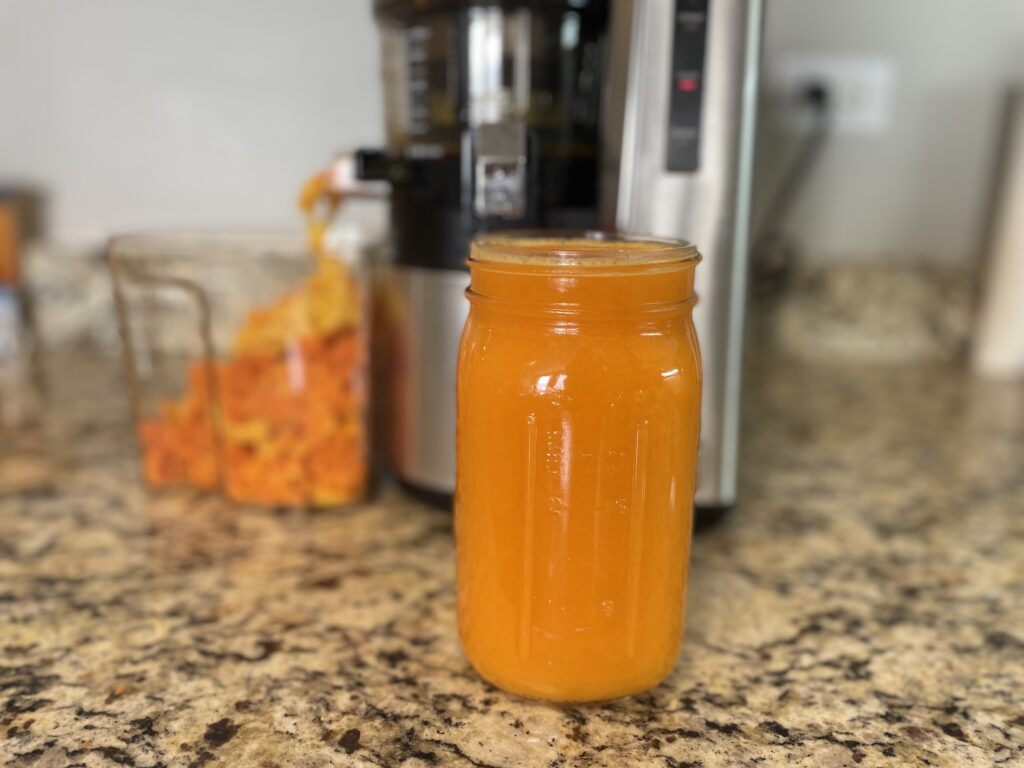 orange juice filled to the top of a mason jar, with juicer behind it