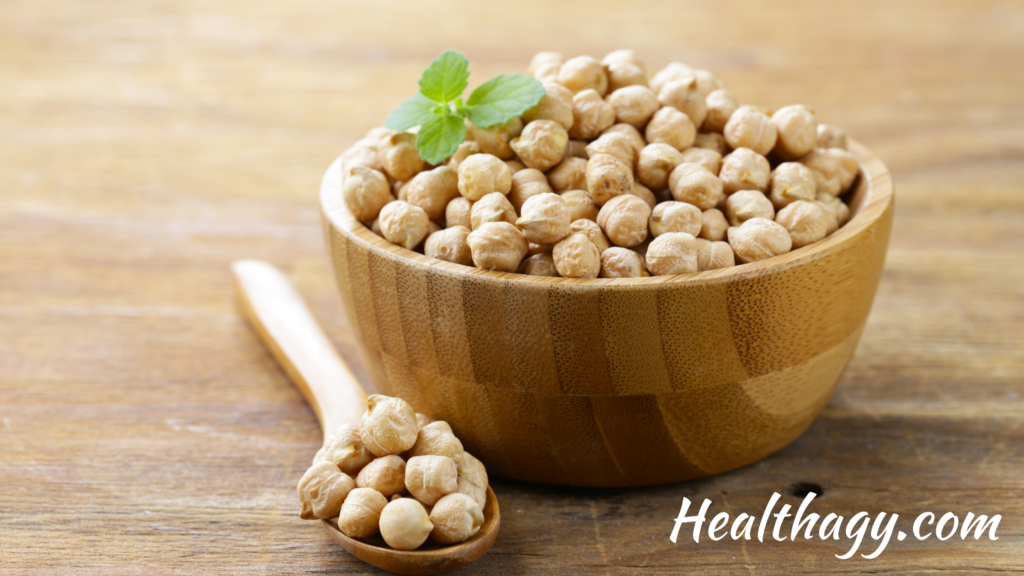 wooden bowl full light tan chickpeas, a spoon full of chickpeas rests next to the bowl