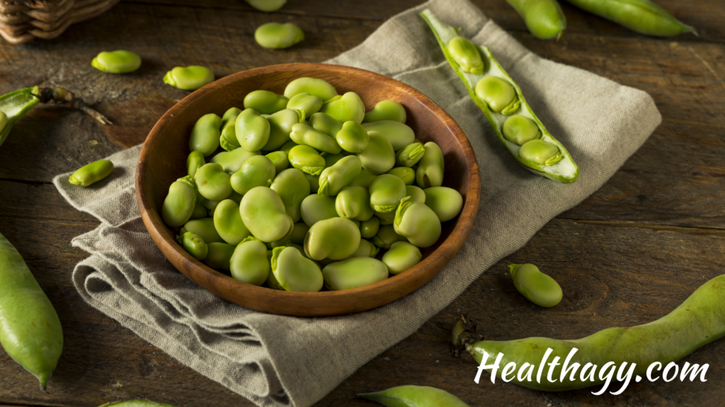 bowl of green fava beans, next to fava bean pods