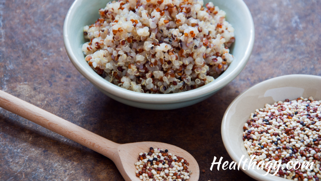 fluffy cooked quinoa in bowl, quinoa seeds in spoon and smaller bowl next to the bowl of cooked quinoa