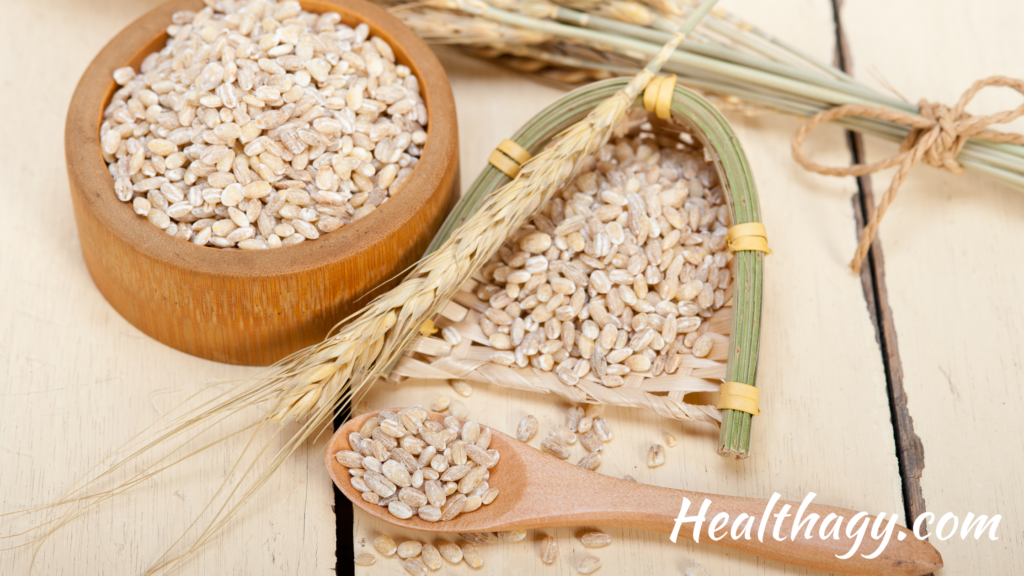 barley grains in a wood bowl and on a wood spoon next to a stalk of barley grass